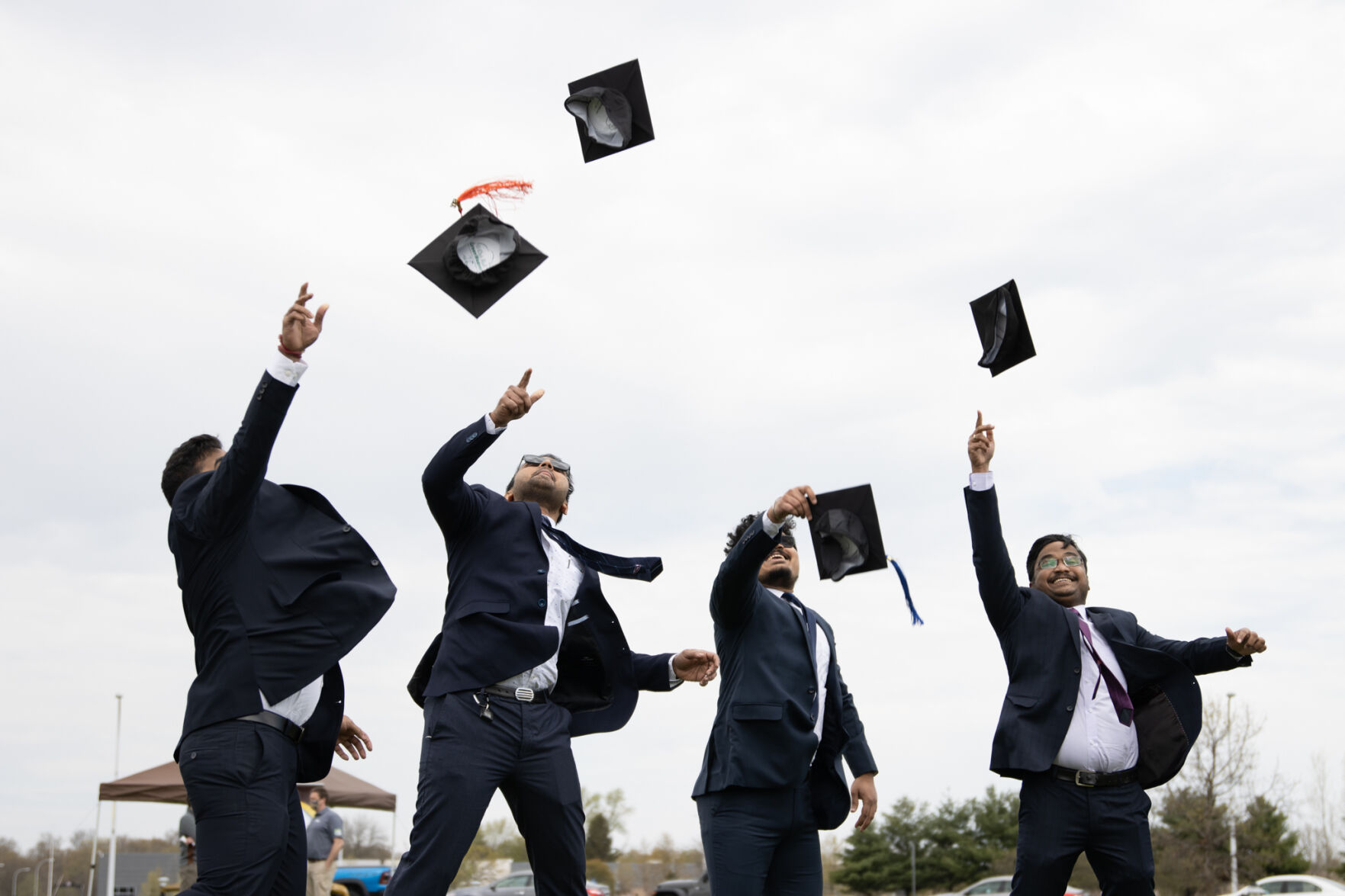 A group of graduates throw their caps in the air on the lawn outside of Floyd Hall.